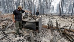 Adam Bailey, left, looks through the still smoldering remains of his home as his father-in-law Joel Miller looks on Monday, Sept. 14, 2015, in Cobb, Calif. Bailey escaped the flames with his baby Saturday, just before flre roared through the neighborhood of about two dozen homes. Two of California's fastest-burning wildfires in decades overtook several Northern California towns, killing at least one person and destroying hundreds of homes and businesses and sending thousands of residents fleeing highways lined with buildings, guardrails and cars still in flames. (AP Photo/Elaine Thompson)