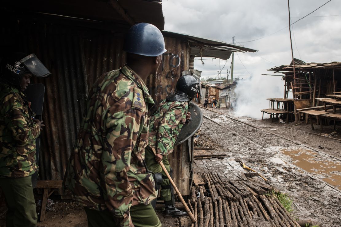 Police peer around a building after throwing tear gas at stone-throwing protesters in Kibera. 