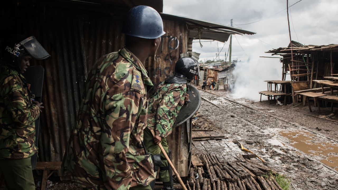 Police peer around a building after throwing tear gas at stone-throwing protesters in Kibera.