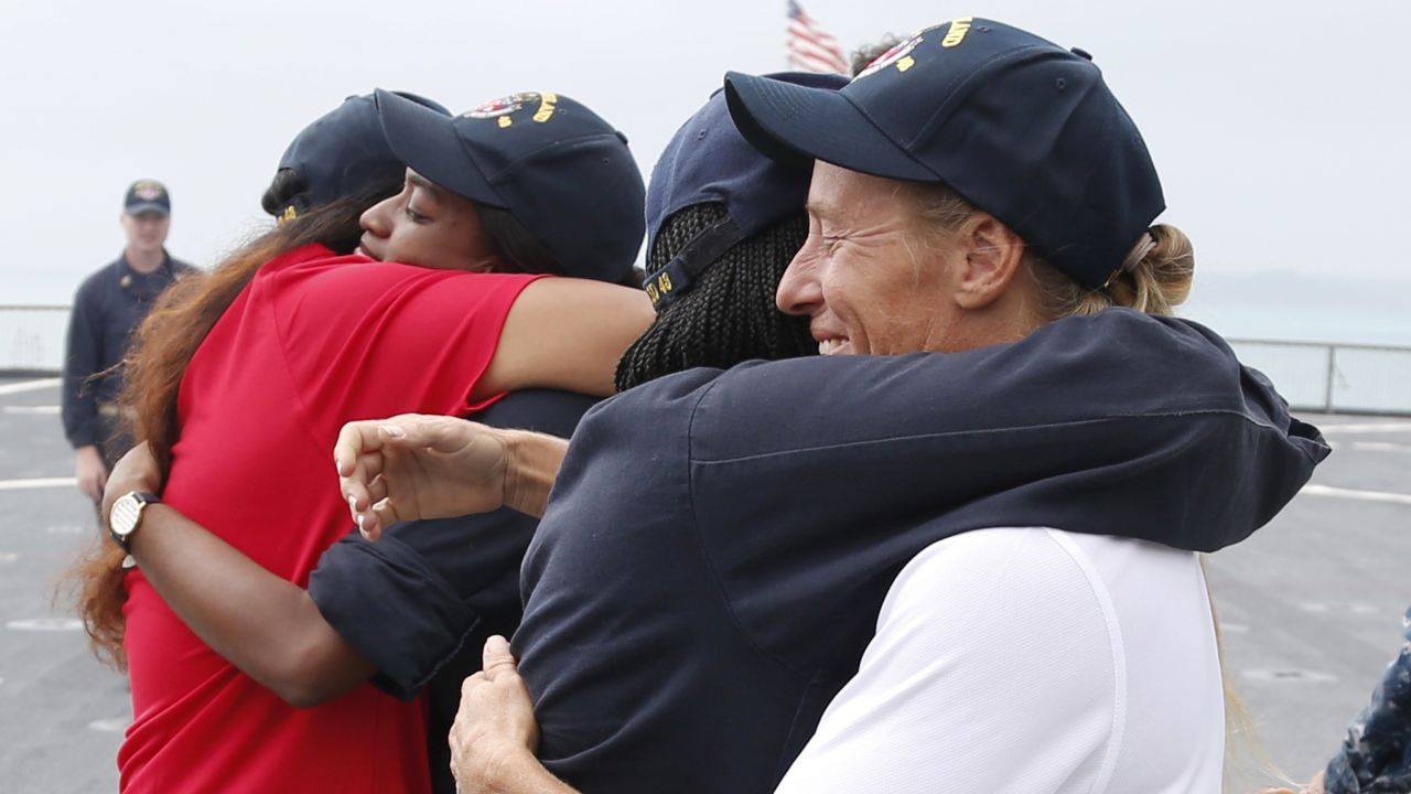 Jennifer Appel, right, and Tasha Fuiava hug crew members of the USS Ashland on the ship's deck.