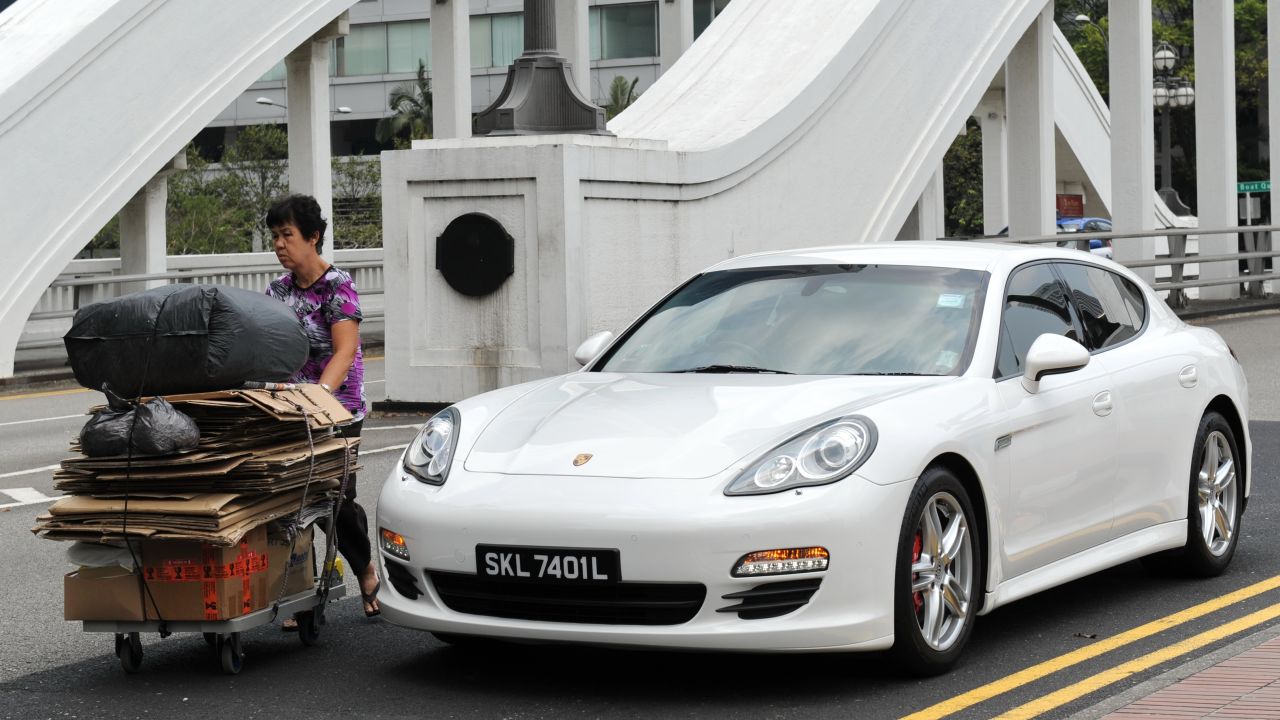 A woman pushes a trolly of recycle waste past a luxury car on the street in Singapore on march 4, 2014.