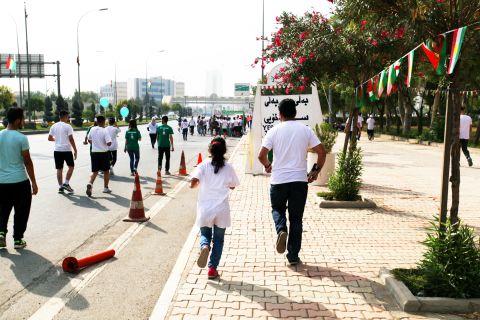 A father and daughter team run past signs advocating Kurdish independence.