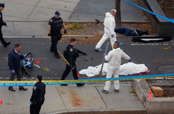 Police officers stand next to a body covered under a white sheet. The driver of the truck drove the wrong way down the West Side Highway bike path for several blocks, according to two senior law enforcement sources at the New York Police Department. After striking multiple people, the driver hit a school bus and wrecked the truck, an NYPD official said.