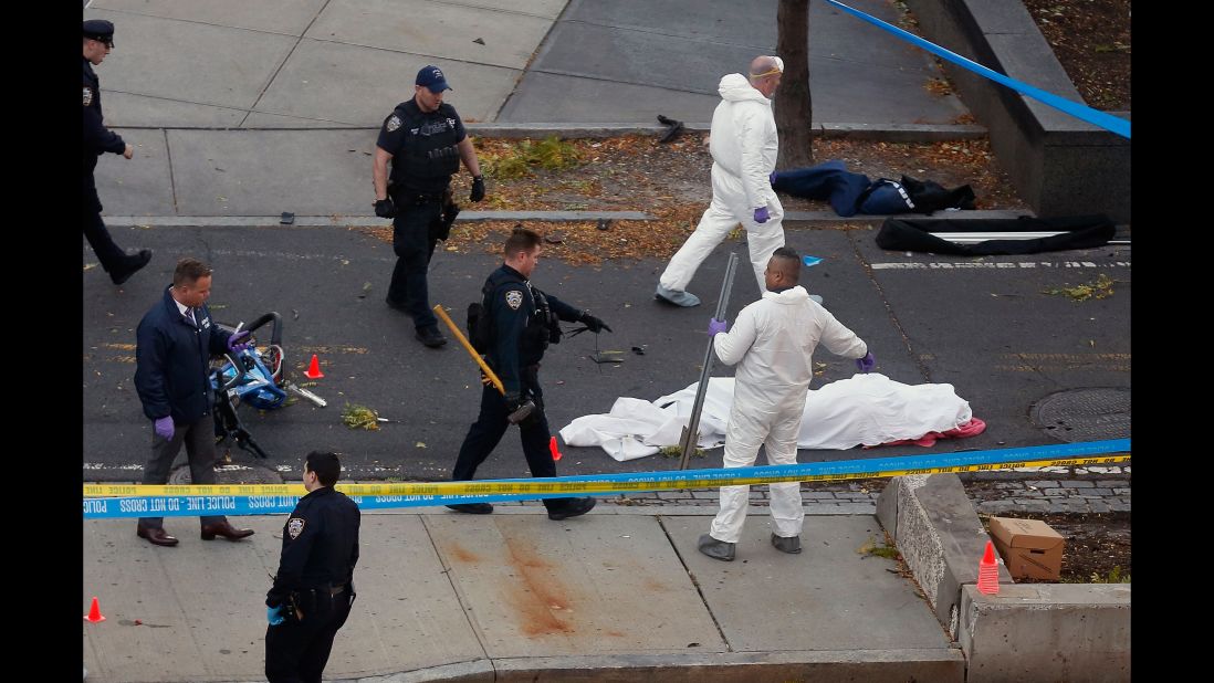 Police officers stand next to a body covered under a white sheet.
