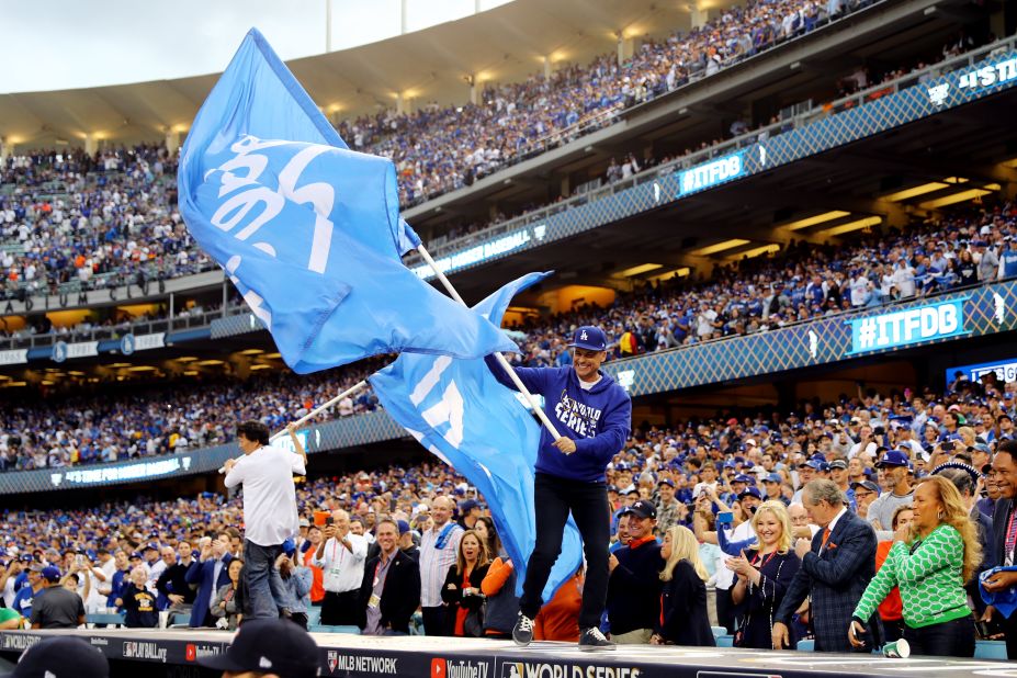 Actors Rob Lowe, right, and Ken Jeong wave Dodger flags on top of a dugout before the game. Many celebrities were in attendance.