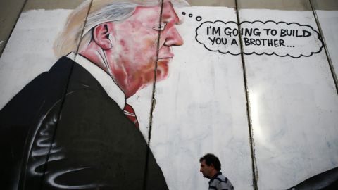 A Palestinian man walks past graffiti depicting President Donald Trump on the controversial Israeli separation wall on August 7, 2017.