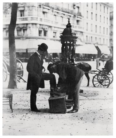 A man has his shoes shined on the streets of Paris, as seen by pioneering French photographer Eugène Atget.