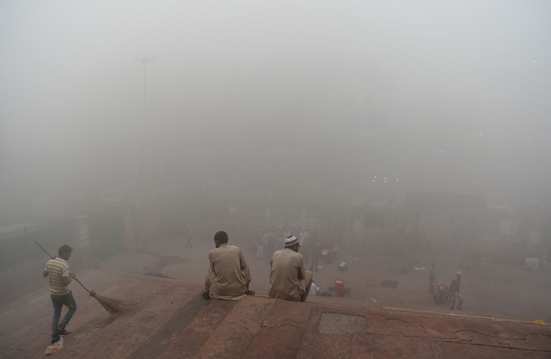 Indian visitors sit on the steps outside Jama Masjid amid heavy smog in the old quarters of New Delhi on November 8, 2017.