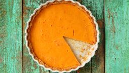 Fresh round bright orange homemade pumpkin pie in white baking dish on turquoise table overhead view