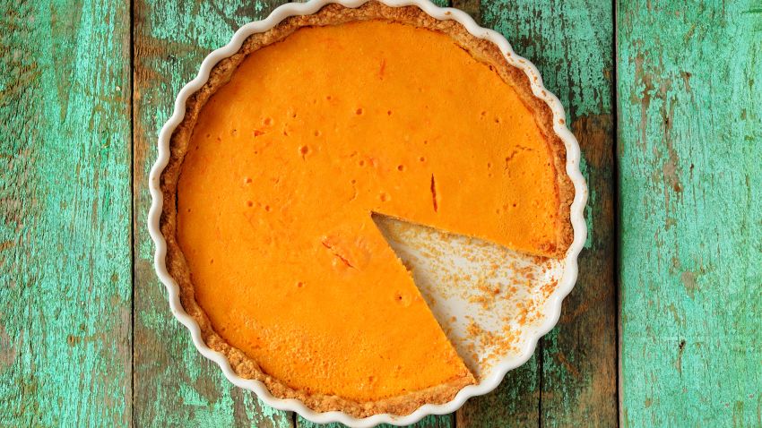 Fresh round bright orange homemade pumpkin pie in white baking dish on turquoise table overhead view