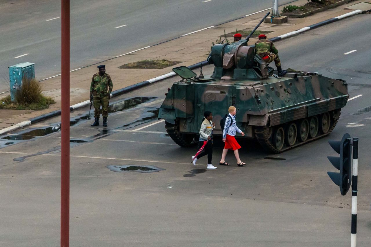 Two pedestrians pass behind an armored personnel carrier stationed at an intersection in Harare on November 15.