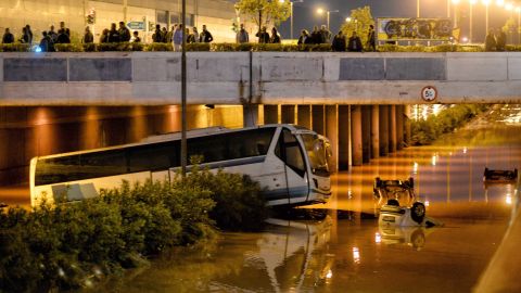 People look on as a bus and cars are submerged Wednesday on a flooded road in Mandra.