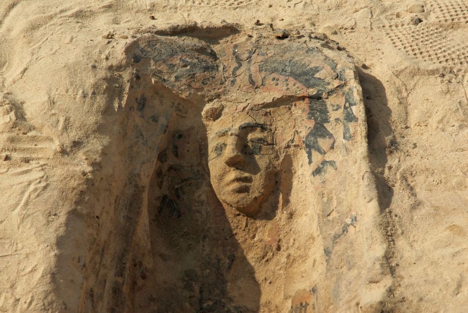 The face mask of a slipper coffin, a form of pottery coffin, stands in relief.  The grave is dated from the Late Period and is situated south of the Wall of  the Crow, an ancient stone wall bordering the "workers' town" -- the so-called "Lost City of the Pyramids."