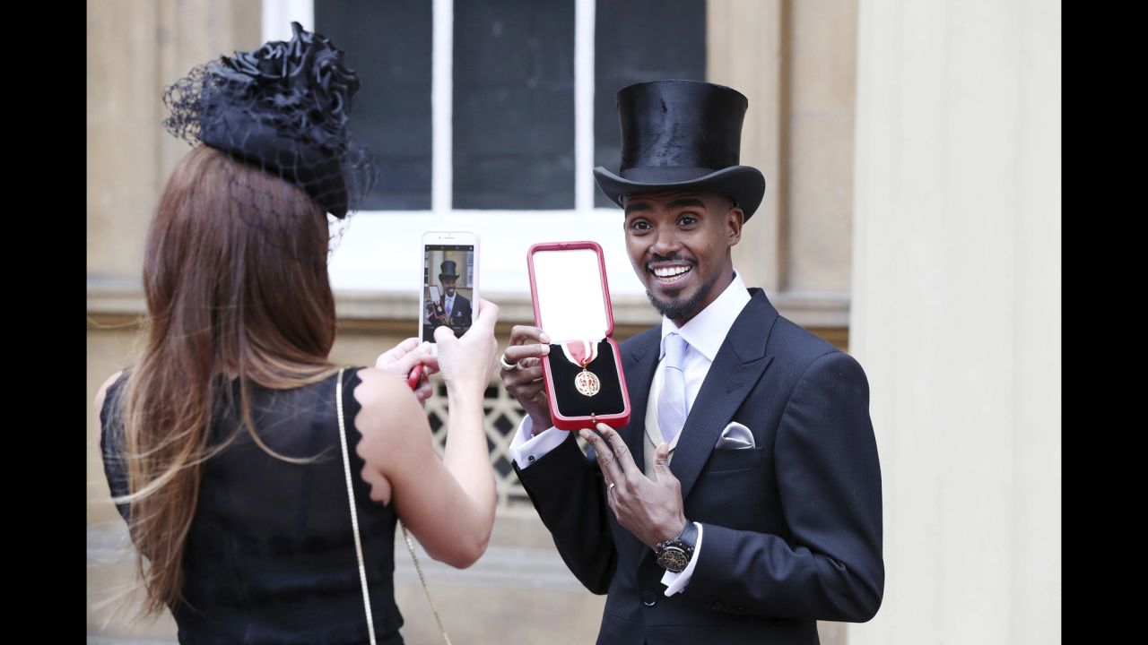 British track star Mo Farah poses for his wife, Tania, after being awarded a knighthood by Queen Elizabeth II on Tuesday, November 14. Farah, a distance runner, has won four Olympic gold medals.
