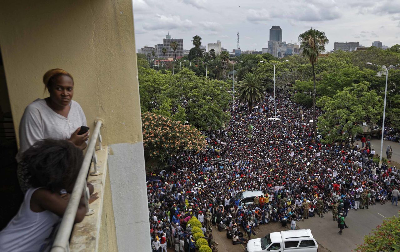 A woman and her daughter look out from their balcony as a crowd of protesters gather on the road leading to the State House in Harare on Saturday, November 18.