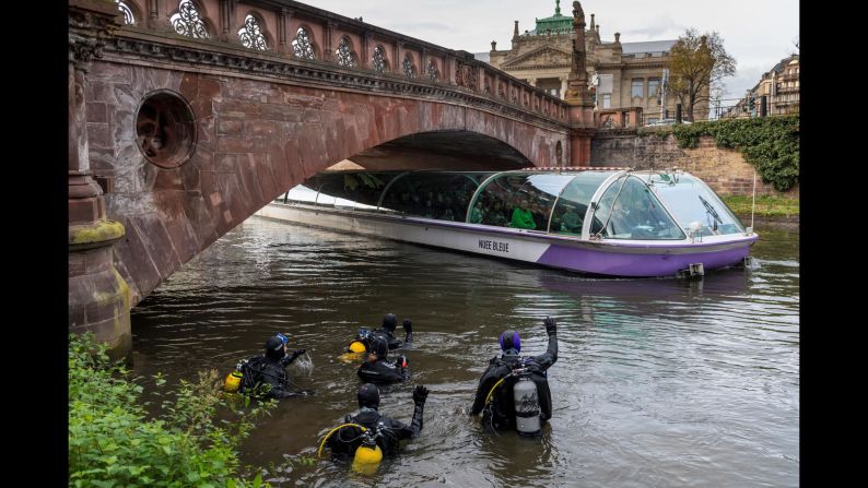 Divers wave at people in a tourist boat as they clean up trash from the Ill river in Strasbourg, France, on Saturday, November 18.
