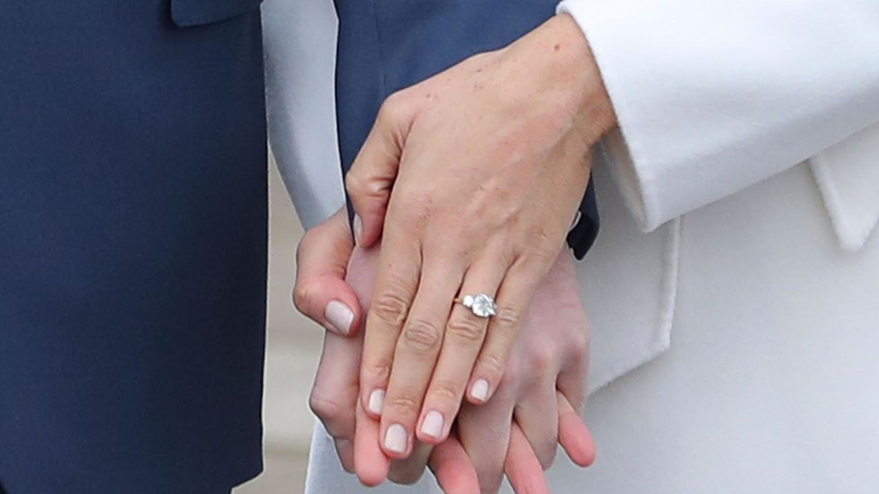 Britain's Prince Harry stands with his fiancée Meghan Markle as she shows off her engagement ring .