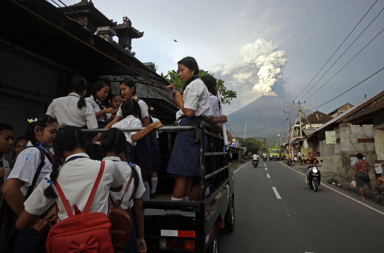 Students stand on a truck on their way to go to school, with erupting Mount Agung in the distance. The National Agency for Disaster Management issued a Level 4 alert on Monday, November 27, indicating the potential for another larger eruption and recommending no public activities within 8 to 10 kilometers from the peak of the volcano.