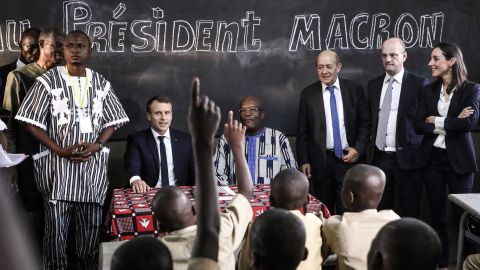 School children rise their hands as French President Emmanuel Macron (left) and Burkina Faso's President Roch Marc Christian Kabore (center) visit a school Tuesday in Ouagadougou.