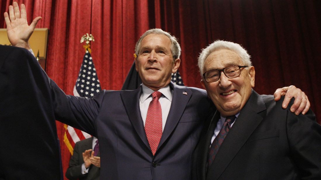 Kissinger stands with President George W. Bush in New York after Bush spoke about the economy in 2008.