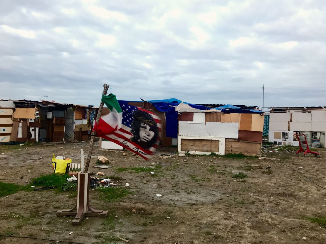 A US flag bearing Jim Morisson's face flies next to an Italian flag, amid the makeshit homes of the "Runway Ghetto," in Foggia.