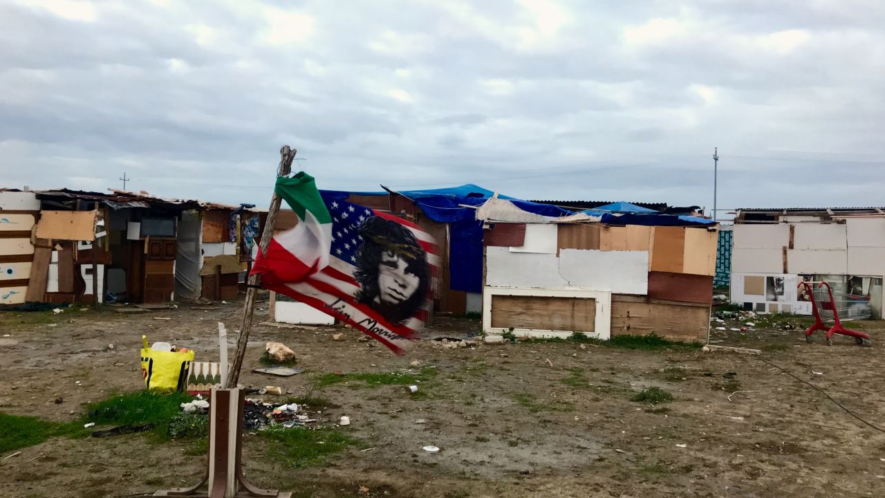 A US flag bearing Jim Morisson's face flies next to an Italian flag, amid the makeshit homes of the "Runway Ghetto," in Foggia.