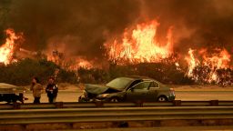A woman involved in a traffic accident waits to get towed beside a wall of flames on the 101 highway during the Thomas wildfire near Ventura, California on December 6, 2017. 
California motorists commuted past a blazing inferno Wednesday as wind-whipped wildfires raged across the Los Angeles region, with flames  triggering the closure of a major freeway and mandatory evacuations in an area dotted with mansions. / AFP PHOTO / Mark RALSTON        (Photo credit should read MARK RALSTON/AFP/Getty Images)