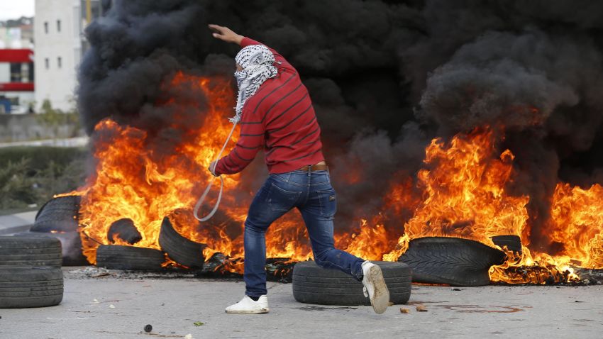 A Palestinian demonstrator runs past burning tires during clashes with Israeli troops during protests in the West Bank city of Ramallah on December 7