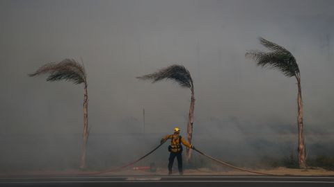 Palm trees sway in a gust of wind as a firefighter carries a hose in Ventura on December 7.
