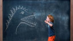 Young boy roaring at dinosaur drawing on blackboard