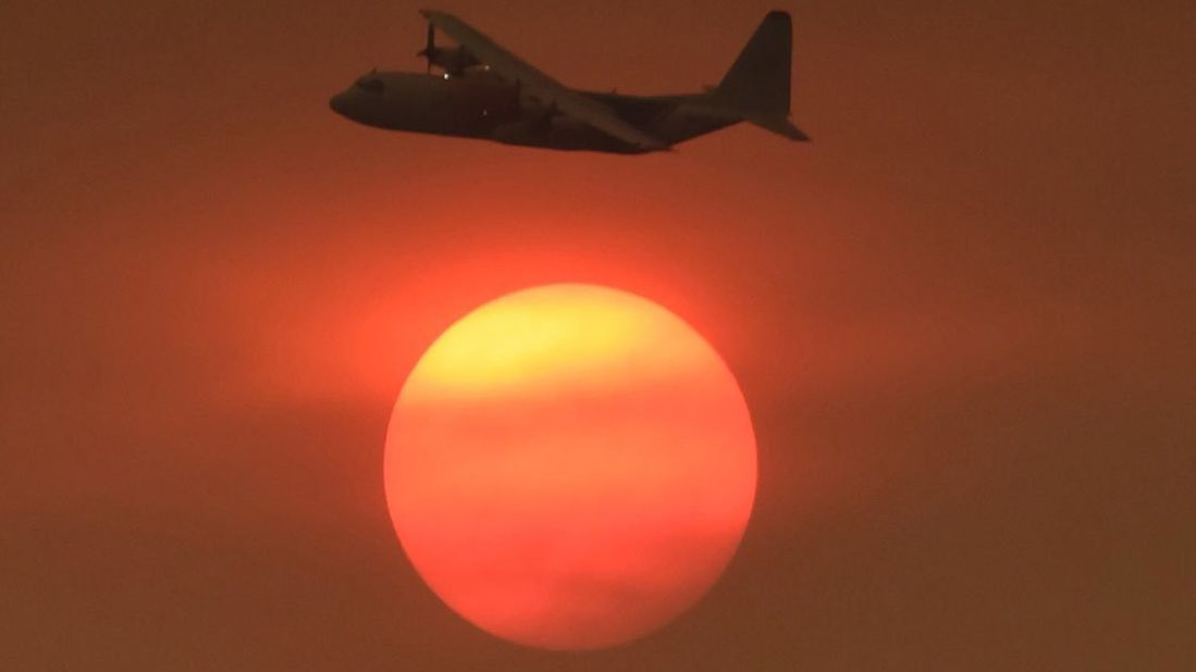 As smoke obscures the sun, a Coulson C-130 air tanker turns to make a drop on a Carpinteria hillside on December 11.