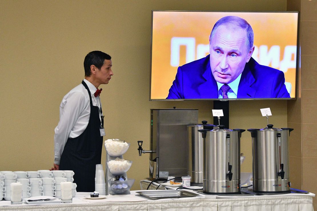 A waiter stands by a screen broadcasting Putin's marathon annual press conference in Moscow on Thursday.