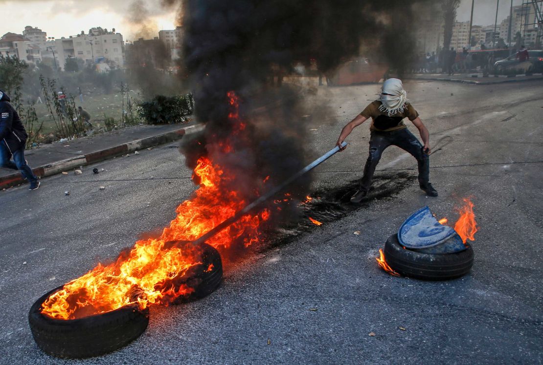 A Palestinian protester uses a stick to move flaming tires during clashes with Israeli forces on the outskirts of Ramallah on Friday. 