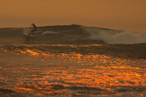 A smoke-filled sky filters sunlight to orange around a surfer as the Thomas Fire continues to grow and threaten communities from Carpinteria to Santa Barbara on Tuesday, December 12, in Carpinteria, California.