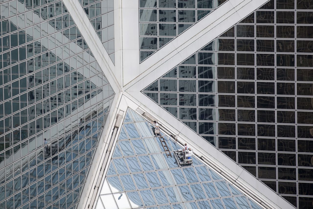 Men clean windows on the Bank of China Tower in 2014. The tower's exterior is clad in reflective glass that mirrors its surroundings.  