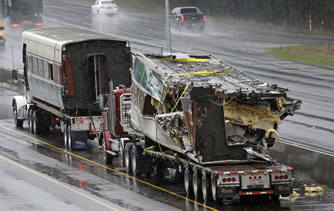 Two damaged train cars sit on flatbed trailers after being taken from the train crash scene on I-5.