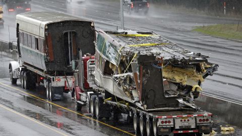 Two damaged train cars sit on flatbed trailers after being taken from the train crash scene on I-5.