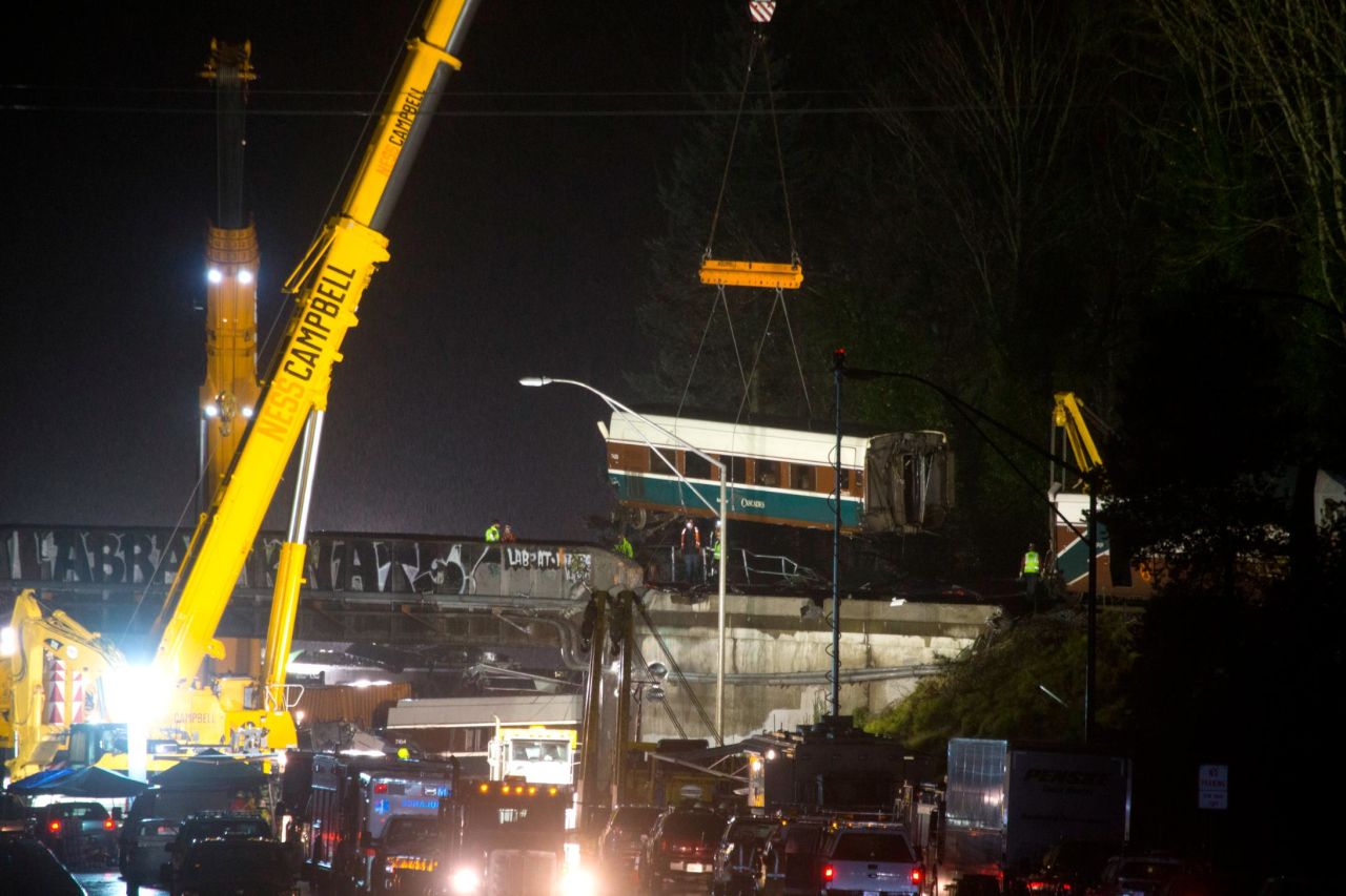 A train car is lifted away on Tuesday, December 19, the day after an Amtrak passenger train derailed near DuPont, Washington. Several of the train's cars spilled off an overpass and onto Interstate 5.