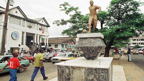 Monrovian pedestrians on Broad Street look up at a statue of George Weah, arguably Liberia's most famous son.