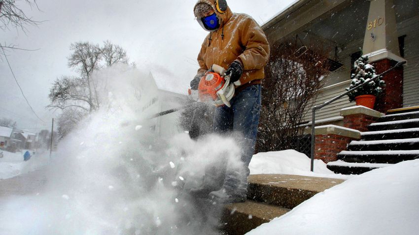 Jose Nieto uses a leaf blower to clear snow from the steps of a sick neighbor during a snowstorm, Friday, Dec. 29, 2017, in Bloomington, Ill. A snow mask and hearing protection allowed him to do his driveway and sidewalks as well. (David Proeber/The Pantagraph via AP)