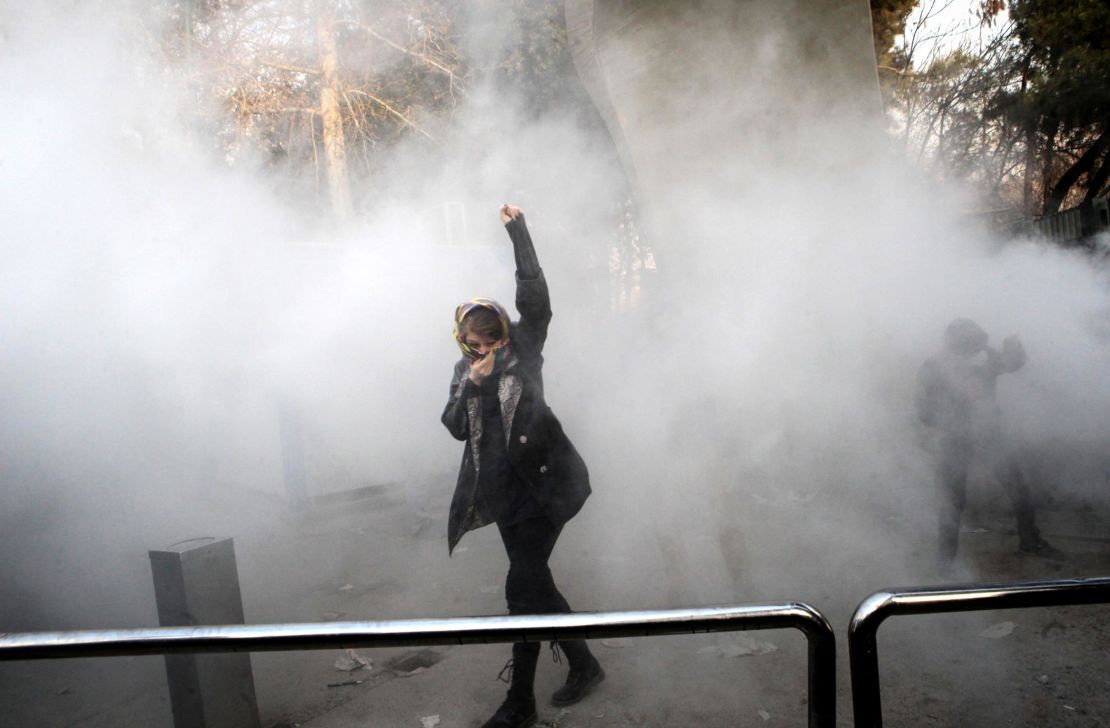 An Iranian woman raises her fist as she makes her way through a cloud of tear gas.