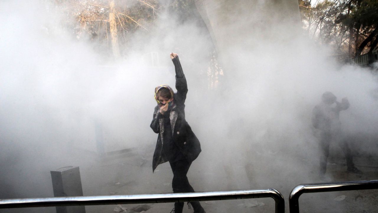 An Iranian woman raises her fist as she makes her way through a cloud of tear gas.