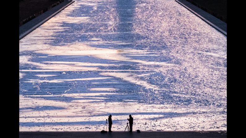 Two photographers are silhouetted against the frozen surface of the Reflecting Pool in Washington as they capture the first sunrise of the new year.