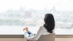 Quality of life concept of business woman rear view relaxing sitting in rest on armchair in modern hotel guest room or luxury home living room looking outward to city urban scene; Shutterstock ID 672164257; Job: -