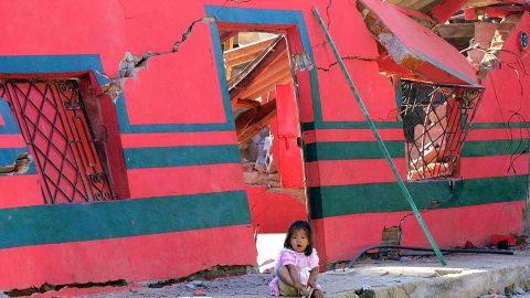 A girl sits in front of a building destroyed by the January 2001 earthquake in San Agustin, El Salvador.