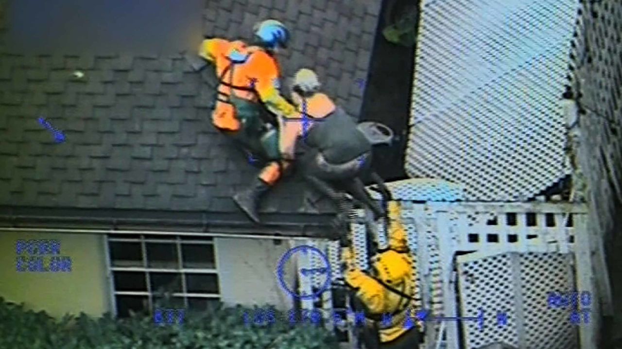 The Coast Guard crew pulls a person onto the roof after a river of mud flowed through the house.