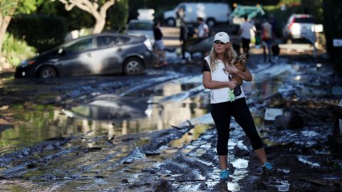  A resident carries her dog as she walks on a mud-covered road after a mudslide on January 10, 2018, in Montecito, California. 
