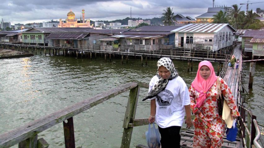 Two women make their way home through Kampong Ayer water village at dusk as the Sultan Omar 'Ali Saifuddien mosque (back-L) is illuminated, in the city of Bandar Seri Begawan, 14 November 2000, the scene of this week's Asia Pacific Economic Cooperation (APEC) forum.  World leaders from the Asia-Pacific region's flagship 21-member economic forum are meeting in the conservative Islamic sultanate of Brunei 15-16 November.     AFP PHOTO/Romy GACAD        (Photo credit should read ROMEO GACAD/AFP/Getty Images)