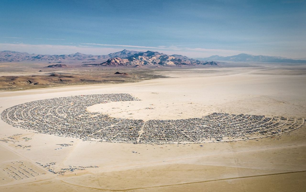 An aerial shot of Black Rock City, where Burning Man takes place each year. The horseshoe-shaped city houses over 70,000 visitors for the nine-day event. The settlements lie around the edge, the Man effigy that is burned at the end of the week stands in the center, and the temple is positioned at the opening of the semi-circle -- the last man-made structure before the expanse of desert beyond.