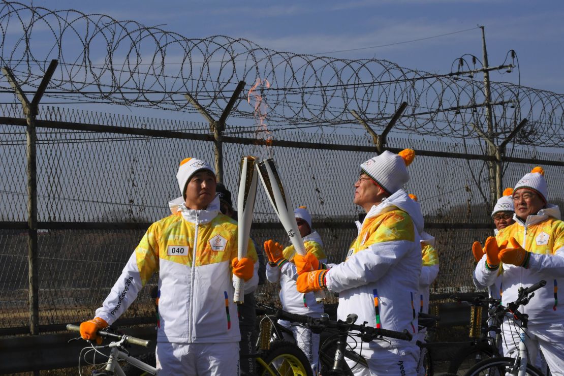 Torchbearers 'kiss' with their torches to pass the Olympic flame in front of a military fence on the road leading to the Panmunjom truce village on January 19, 2018.